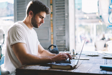 Concentrated serious young freelancer working on completion of new startup and typing on keyboard...
