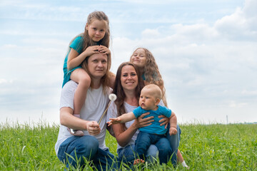 Portrait big family dad, mom and three children on green grass against blue sky. Happy caucasian parents, two daughters and young son.