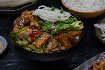 Vegan Japanese rice noodles and stir fried tofu, vegetables, soya  skins on dark table