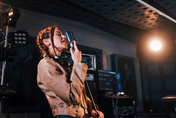 Young beautiful female performer sings and rehearsing in a recording studio