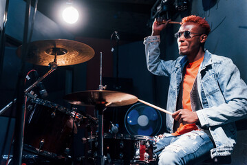 Obraz na płótnie Canvas Plays drums. Young african american performer rehearsing in a recording studio