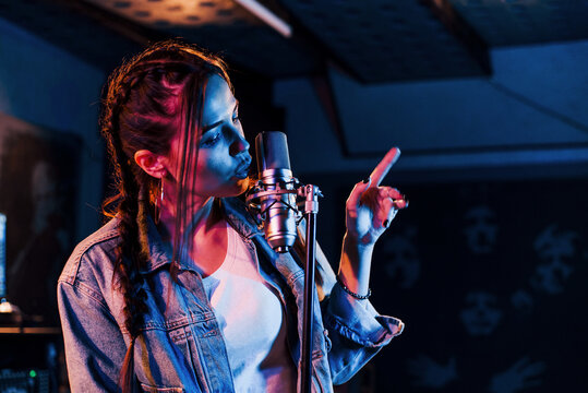 Young beautiful female performer sings and rehearsing in a recording studio