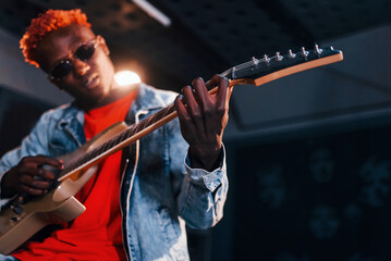 Plays guitar. Young african american performer rehearsing in a recording studio