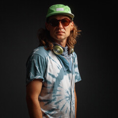 Studio portrait of a young man with long hairs in a green cap and headphones. Black background. Musician DJ