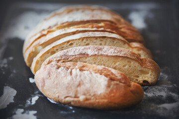 A loaf of sliced fresh white bread lies on a dark baking tray that is stained with flour. Home bread.