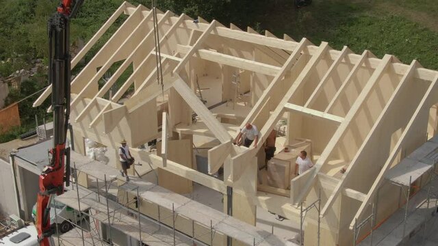 DRONE: Flying near a modern prefabricated house being built in the Slovenian countryside. Group of contractors mounts a wooden arch on the roof of a cross-laminated timber house under construction.