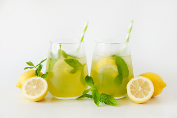 Two glasses of refreshing non alcoholic mojito drink with lemon slices, mint leaves and ice. Studio shot of iced lemonade isolated on white background, close up, copy space.