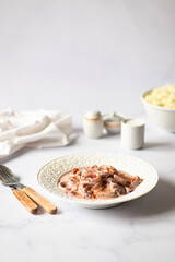 Delicious seafood - squid in a creamy sauce with smoked paprika - served on a white table and light background. Minimalistic composition. Vertical, copy space