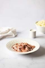 Delicious seafood - squid in a creamy sauce with smoked paprika - served on a white table and light background. Minimalistic composition. Vertical, copy space