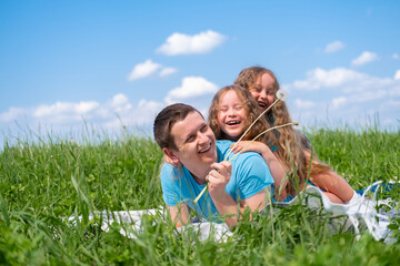 Fototapeta premium Happy father and two little daughters spending time. Dad and daughters playing together on field green grass at summer. 