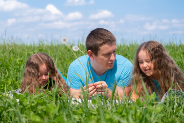 Happy father and two little daughters spending time. Dad and daughters playing together on field green grass at summer. 