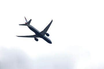 From below of white and blue aircraft flying with cloudy grey sky