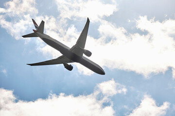 From below of white and blue aircraft flying with blue and cloudy sky