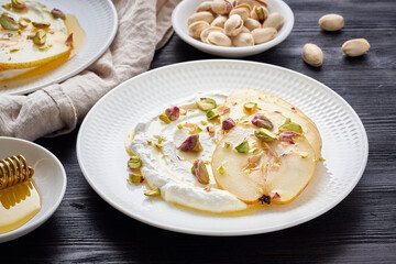 Ricotta with pears, pistachios and honey or maple syrup on two white plate on dark wooden rustic table. Sweet and healthy dessert. Side view