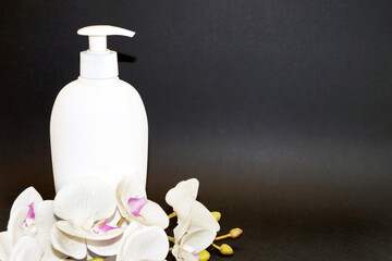 white cosmetic bottle and white orchid flower on a black background close-up