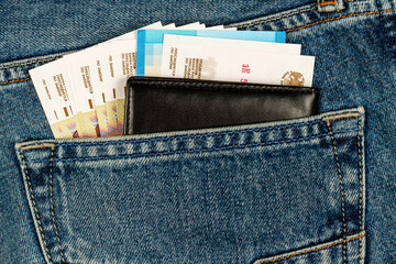 black wallet and banknotes sticking out of blue jeans pocket.