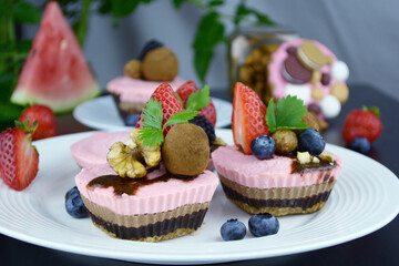 Vegan mini cheesecakes with strawberry and chocolate layer with adding of cashews, cacao butter and coconut milk, and base made of almonds, shredded coconut and dates