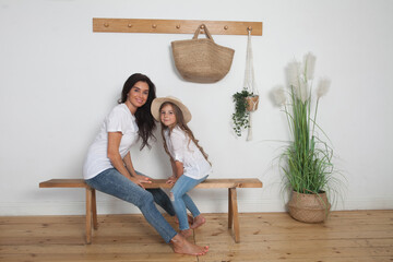 Mother puts on her little daughter a straw hat sitting on a bench in the Scandinavian style interior. Happy loving family having fun at home going for a walk.