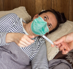 Woman with flu virus lying in bed, measuring  temperature with a thermometer at home