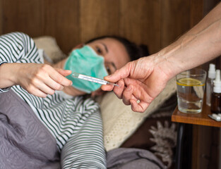 Woman with flu virus lying in bed, measuring  temperature with a thermometer at home