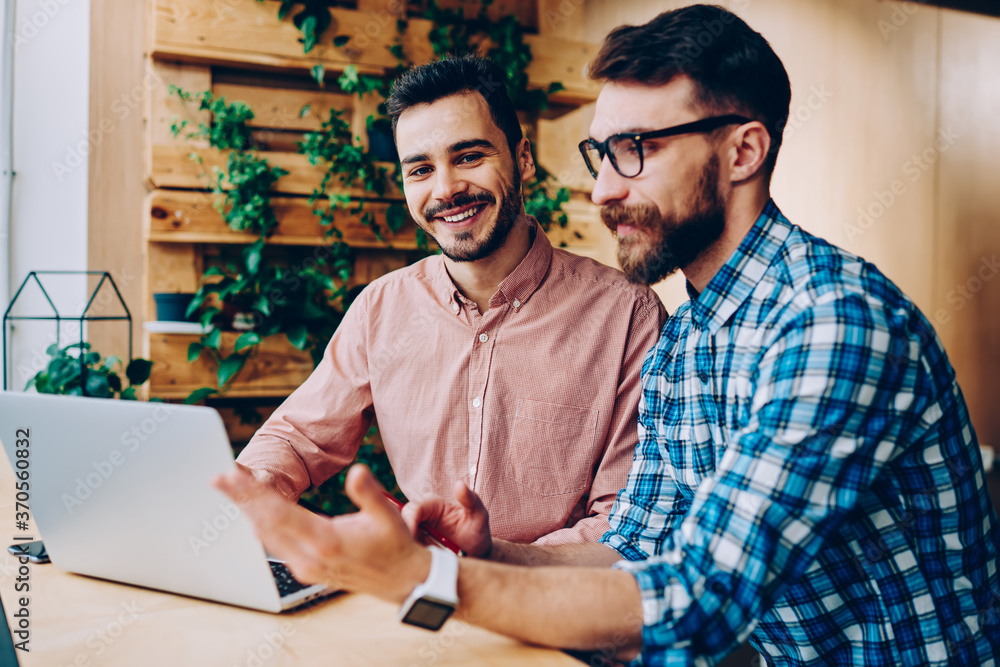 Poster portrait of cheerful handsome man looking at camera while his friend explaining information and idea