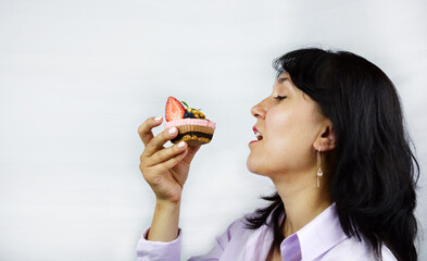 Close up portrait of pretty brunette woman eating tasty cake (raw dessert) with berries and nuts on...