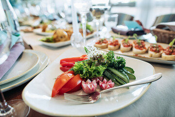 A plate with fresh vegetables on a table in a restaurant. Cucumbers, tomatoes, lettuce