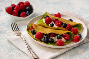 Spinach crepes with cheese , raspberries and blueberries.