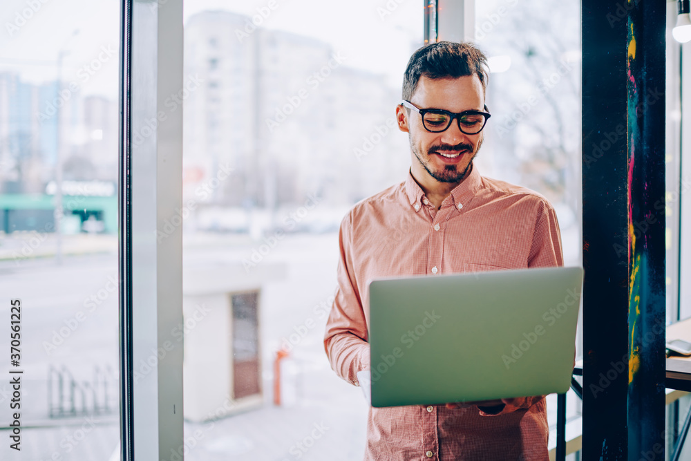 Poster young hipster guy satisfied with spectacles for vision protection reading information from laptop co