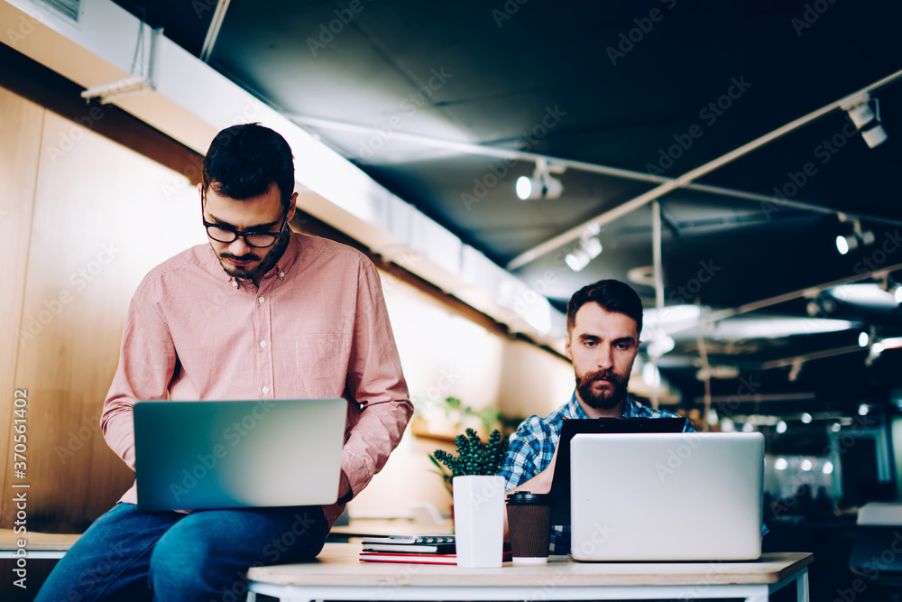 Poster concentrated male it developers working on laptop computers in office, searious young hipster guys p