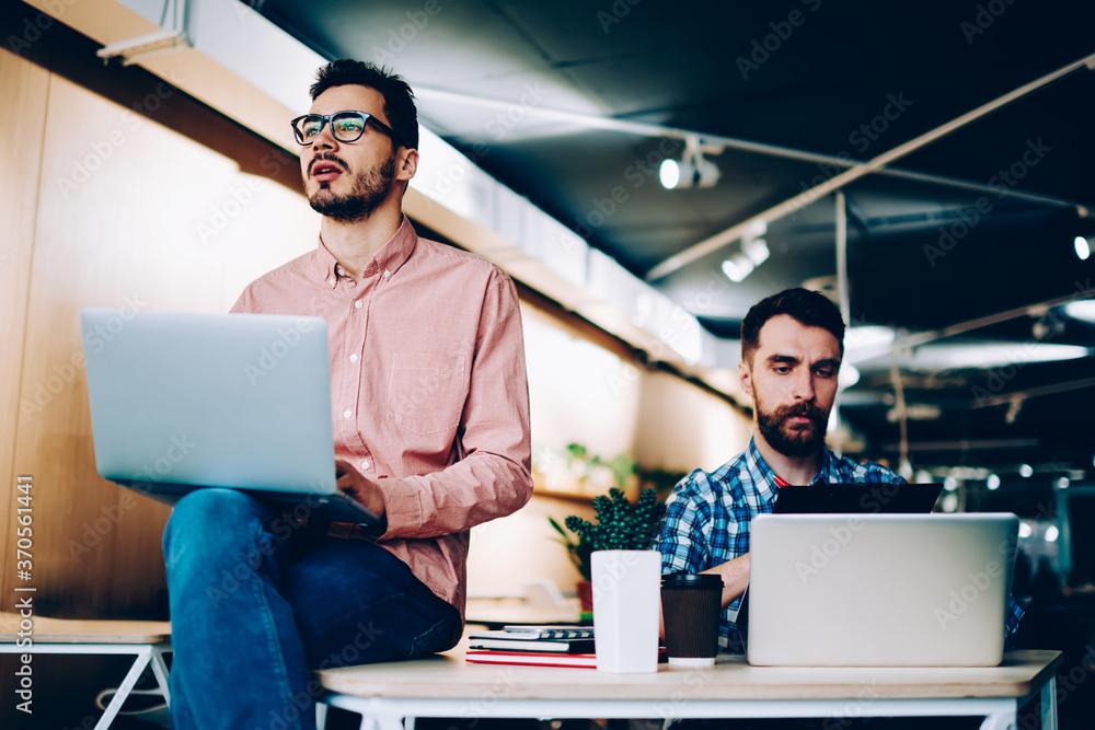 Poster skilled male programmers sitting together in office for completing project making creative solutions