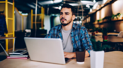 Fototapeta premium Pensive freelancer working at laptop in cafe