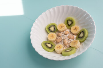 Kiwi, banana, oats and almonds bowl on light green desk. Healthy breakfast concept