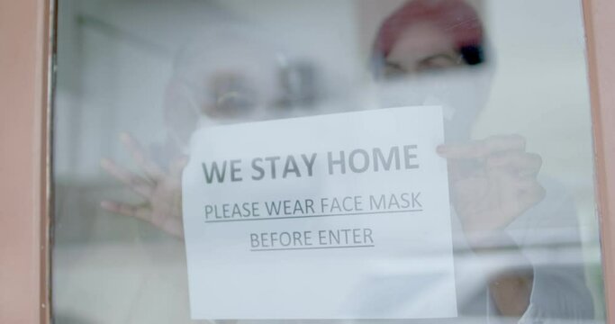 Slow motion of old people sticks up note, paper sign "we stay home, please wear face mask " on window or door, senior protect and warning others as quarantine in house during Coronavirus, Covid-19
