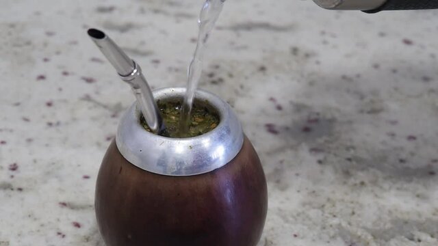 Pouring water in a traditional yerba mate cup with tea leaf. 