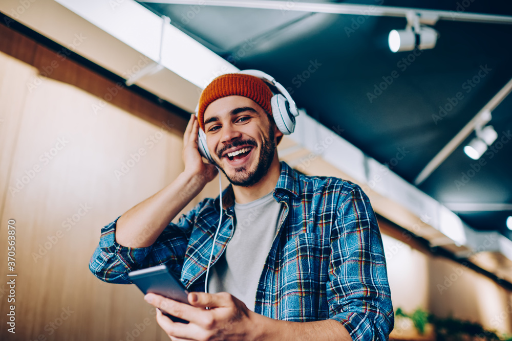 Poster half length portrait of cheerful hipster guy dressed in stylish apparel looking at camera while enjo