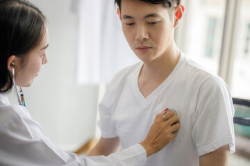 Fototapeta premium Asian female doctor is checking the symptoms of a female patient with a stethoscope in the disease control area. Concepts of care and treatment for patients with COVID 19.