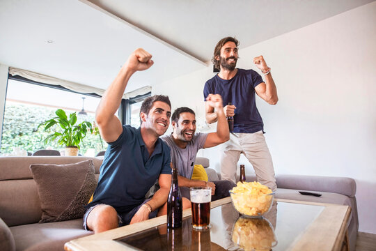 Group of friends watching a game on tv celebrating the victory of their team