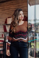 Beautiful model posing for photos in a room. Wearing black pants and brown blouse. 