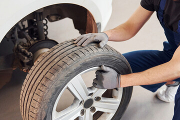 Close up view of man in work uniform with car wheel indoors. Conception of automobile service