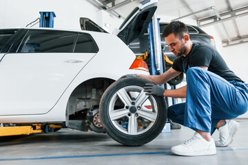 Man in work uniform changing car wheel indoors. Conception of automobile service