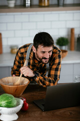 Portrait of handsome man in kitchen. Young man cooking while having video call.