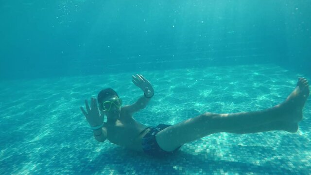 Yoga boy lying on the pool bottom and keeping hands on his nape in slo-mo
