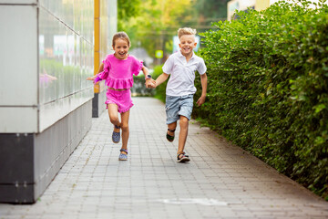 Friends. Two smiling kids, boy and girl running together in town, city in summer day. Concept of...
