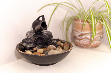 zen water fountian over a white background next to a green plant in a pot