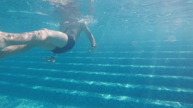 Funny boy swimming backstroke underwater over footsteps in a pool in slo-mo