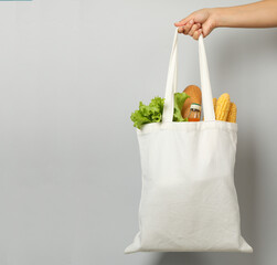 Female hand holds bag with different food on gray background