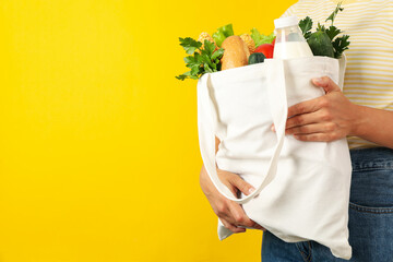 Woman holds bag with different food on yellow background