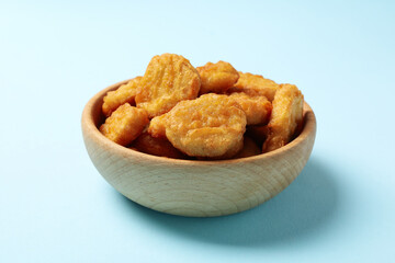 Bowl with fried chicken nuggets on blue background