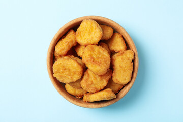Bowl with fried chicken nuggets on blue background